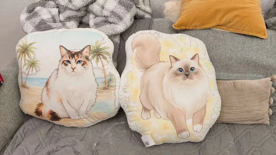 Two custom shaped pillows with watercolor cat artwork on a couch